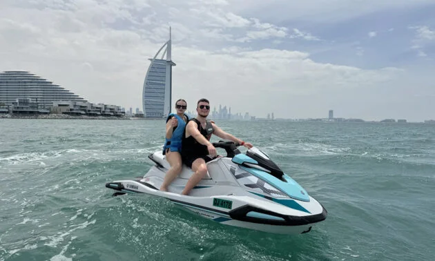 Couple riding a jet ski near Burj Al Arab with the Dubai skyline in the background during a jet ski tour in Dubai.